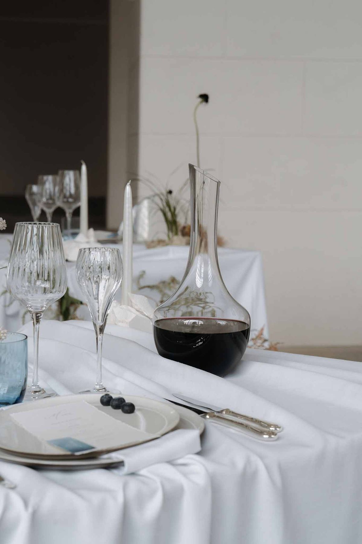 Minimalist place setting with stacked ceramic plates, blueberry garnish, and dusty blue glassware