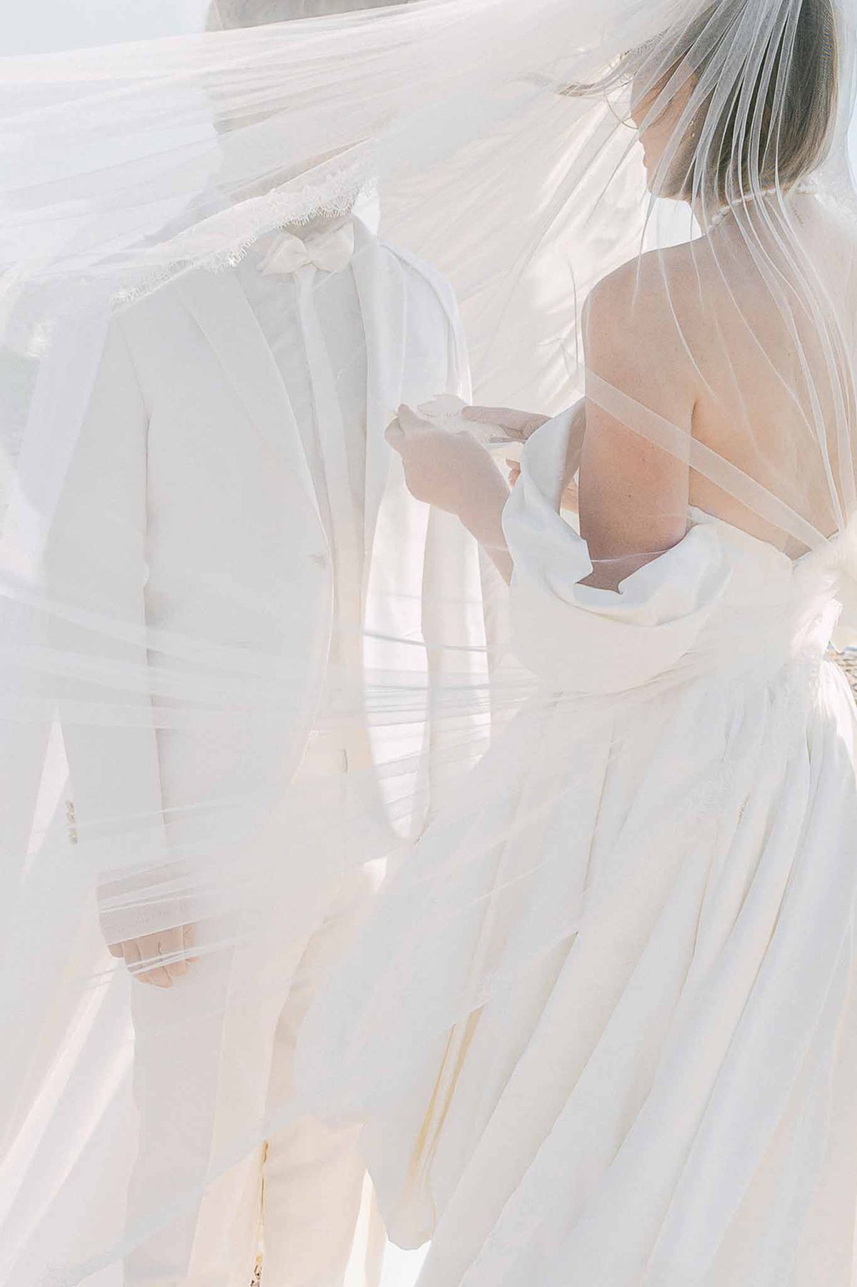 Bride and groom seen through billowing lace-edged veil in high-key close-up outdoor portrait