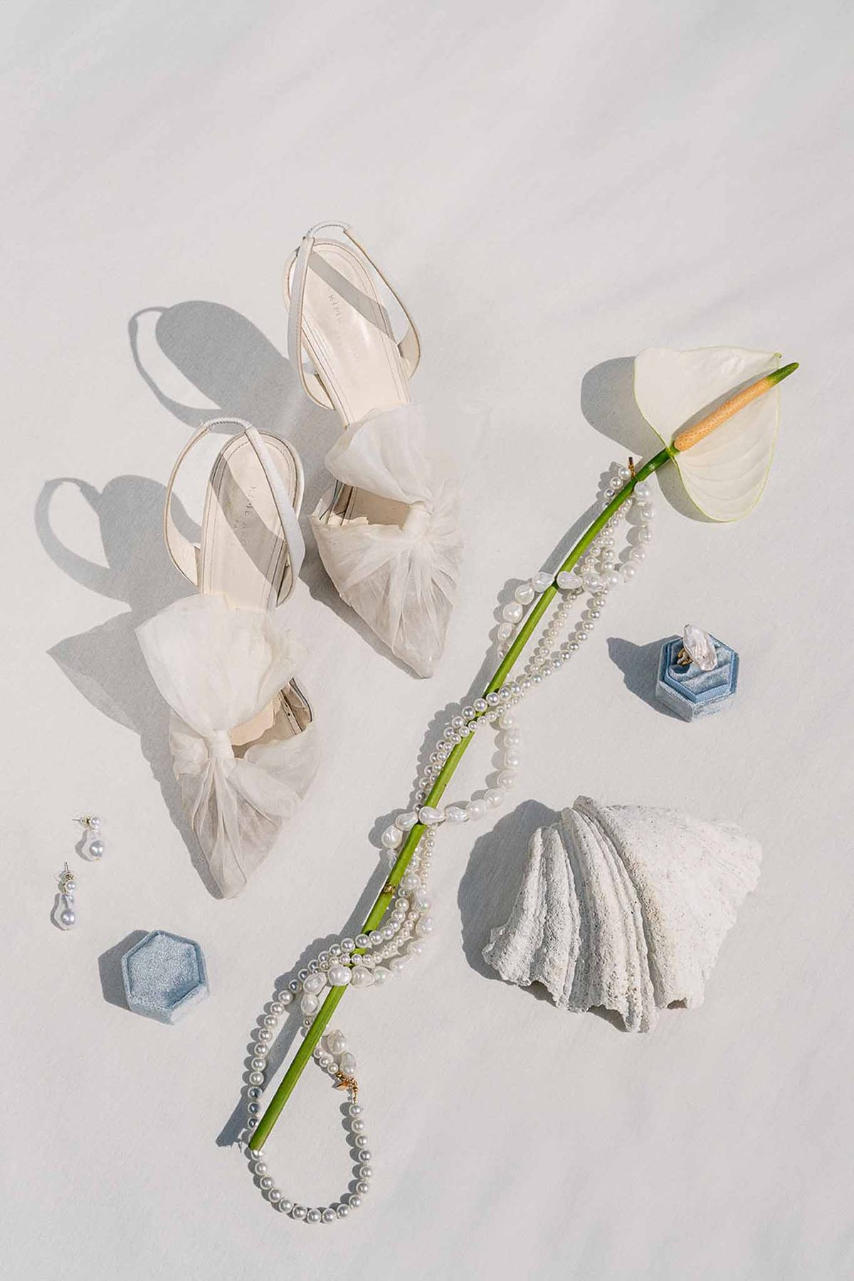 Bridal accessory flat lay with tulle bow heels, pearl necklace, blue velvet ring boxes, and pearl earrings