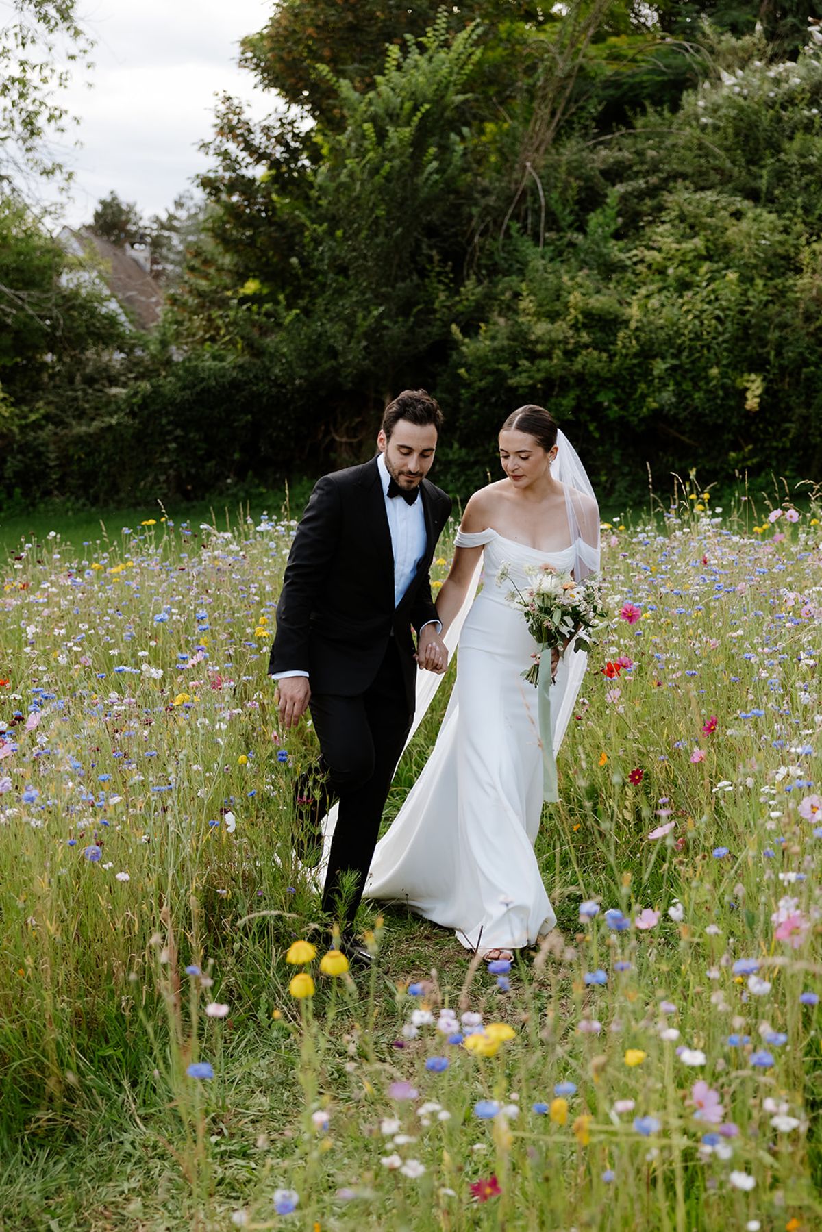 Couple walking hand in hand through wildflower meadow with cornflowers, poppies, and cosmos
