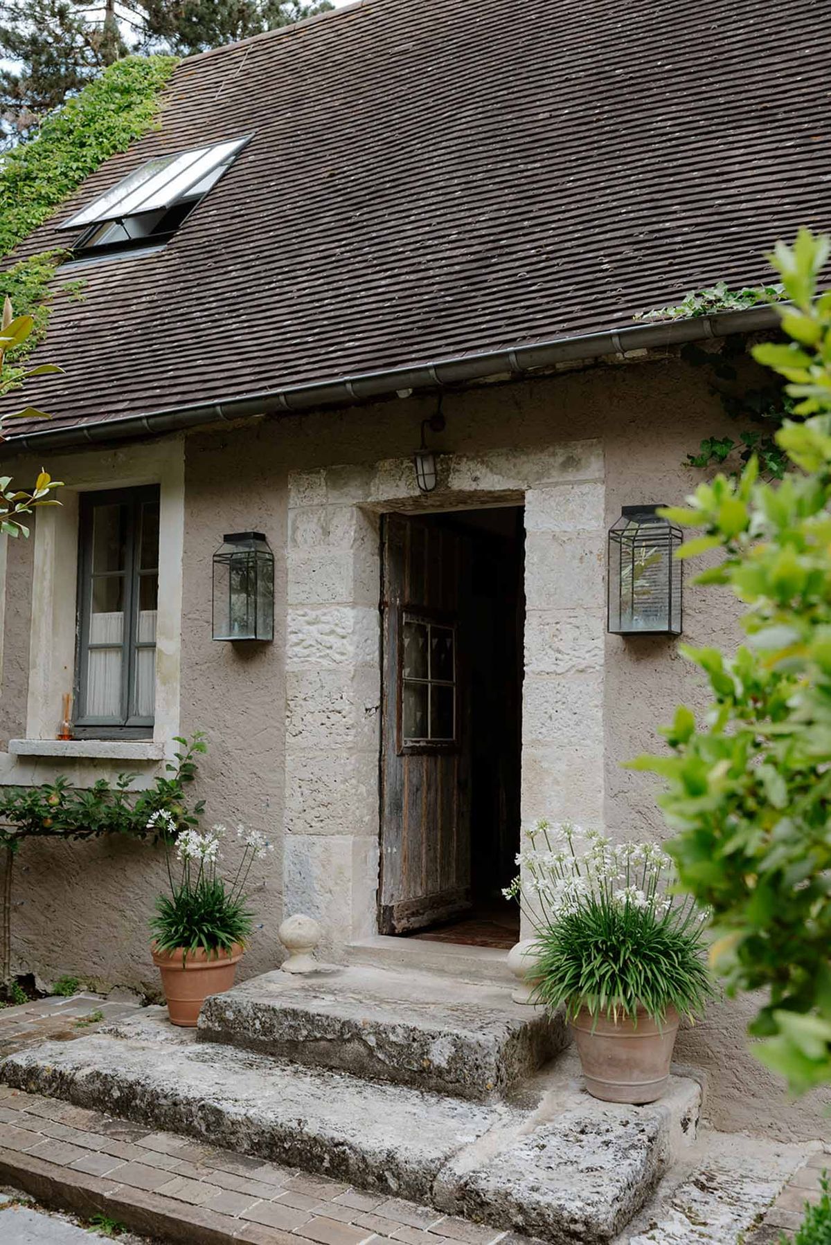 Stone building entrance at Dime de Giverny with wooden door, lantern sconces, and potted white agapanthus