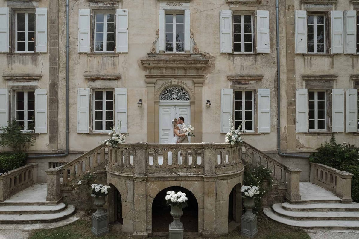 Couple kissing on grand double staircase of chateau decorated with white hydrangea urns