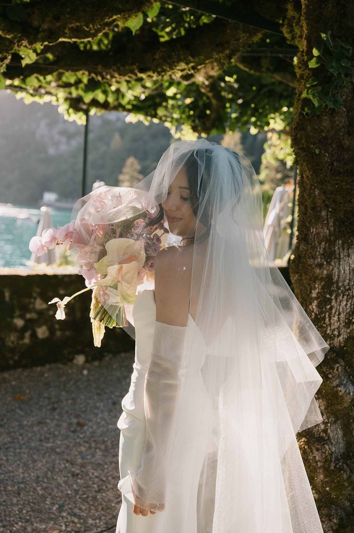 Bride with bouquet under vine pergola with lake behind at Abbaye de Talloires