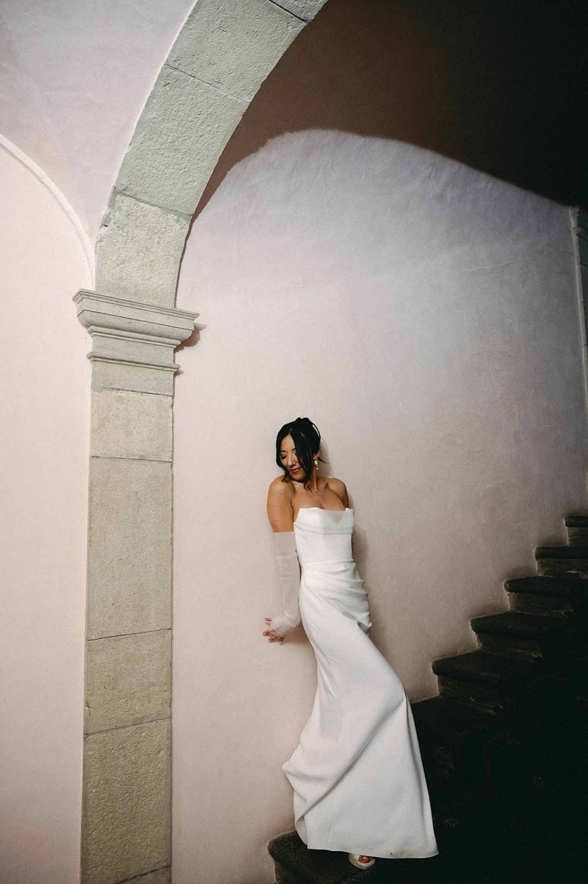 Bride in mermaid gown by stone column and medieval staircase at Abbaye de Talloires