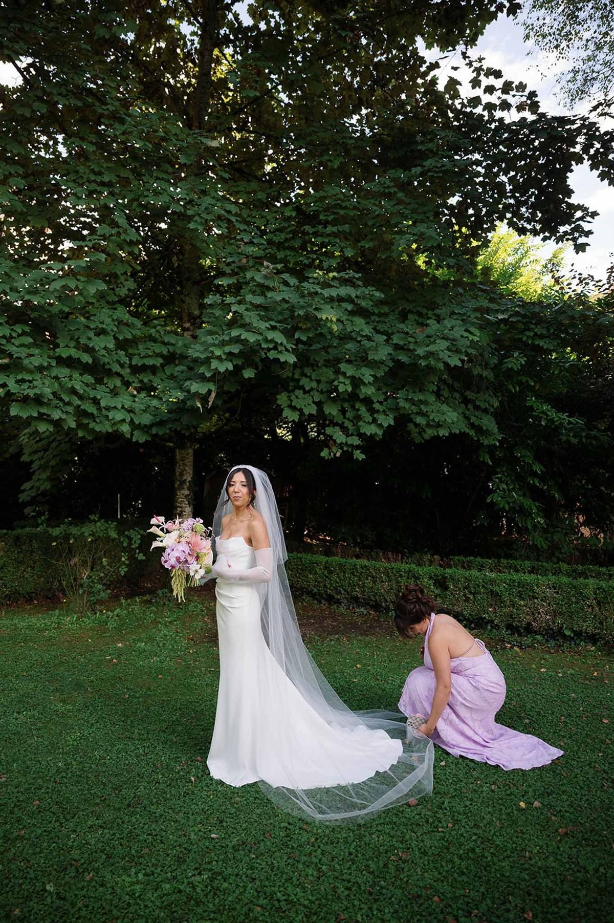 Bridesmaid adjusting bride's veil on lawn at Abbaye de Talloires