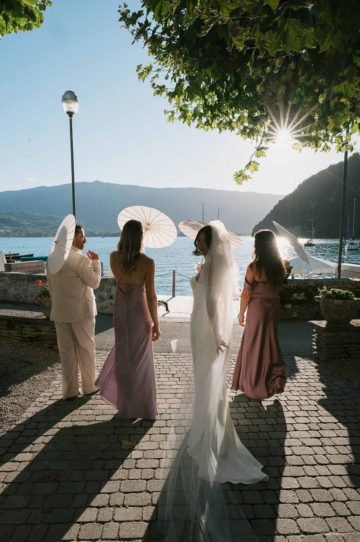 Bride and bridesmaids with parasols walking to Lake Annecy at golden hour at Abbaye de Talloires