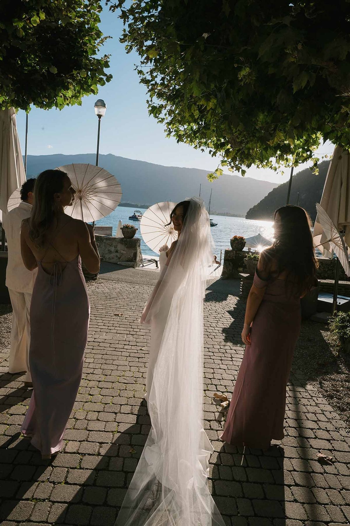 Bride and bridesmaids with parasols on lakeside at sunset at Abbaye de Talloires