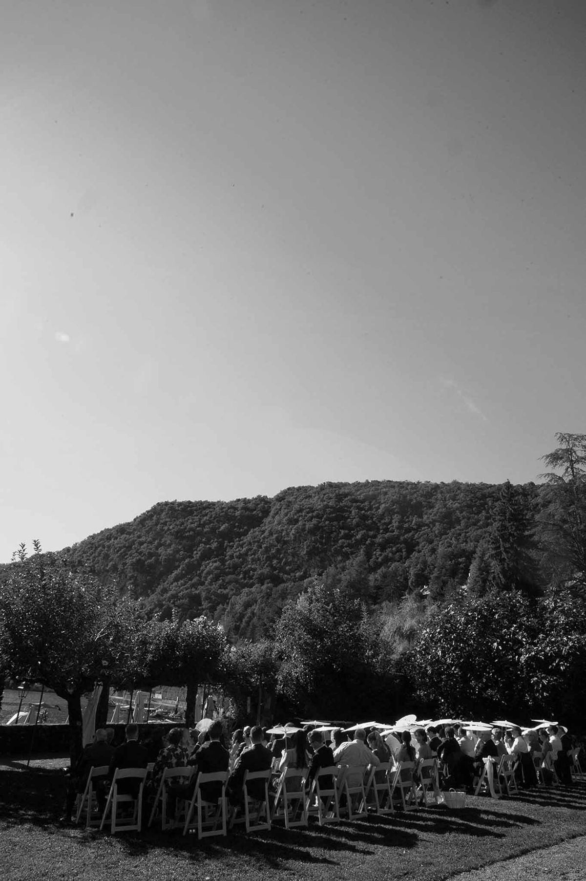 Ceremony guests with parasols and mountain backdrop in black and white at Abbaye de Talloires