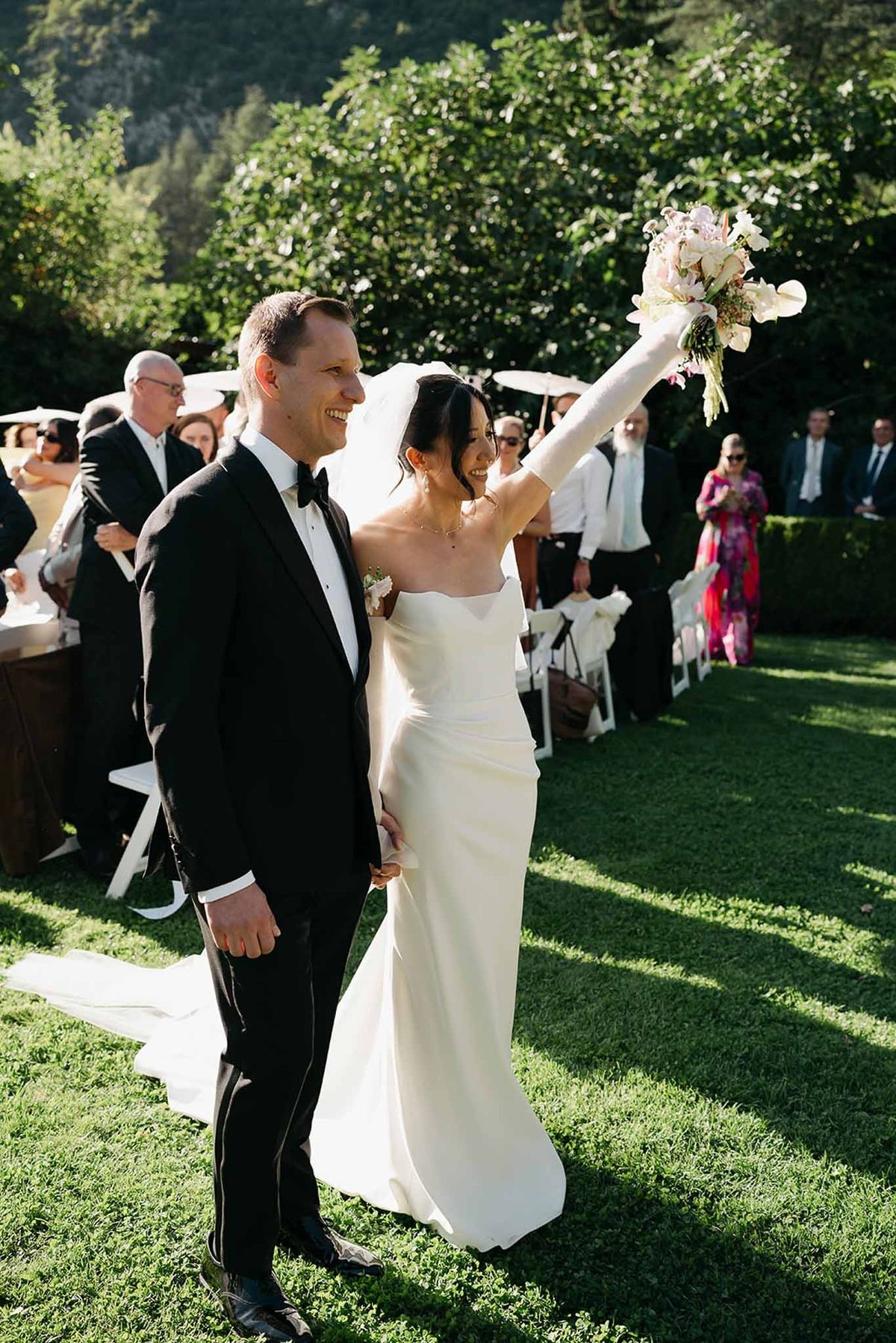 Couple exiting ceremony with bouquet raised and cheering guests at Abbaye de Talloires