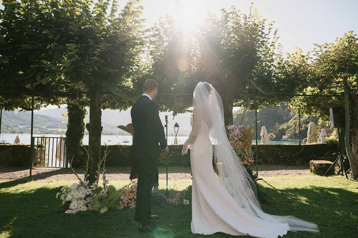 Couple at altar with lake and sunlight streaming through trees at Abbaye de Talloires