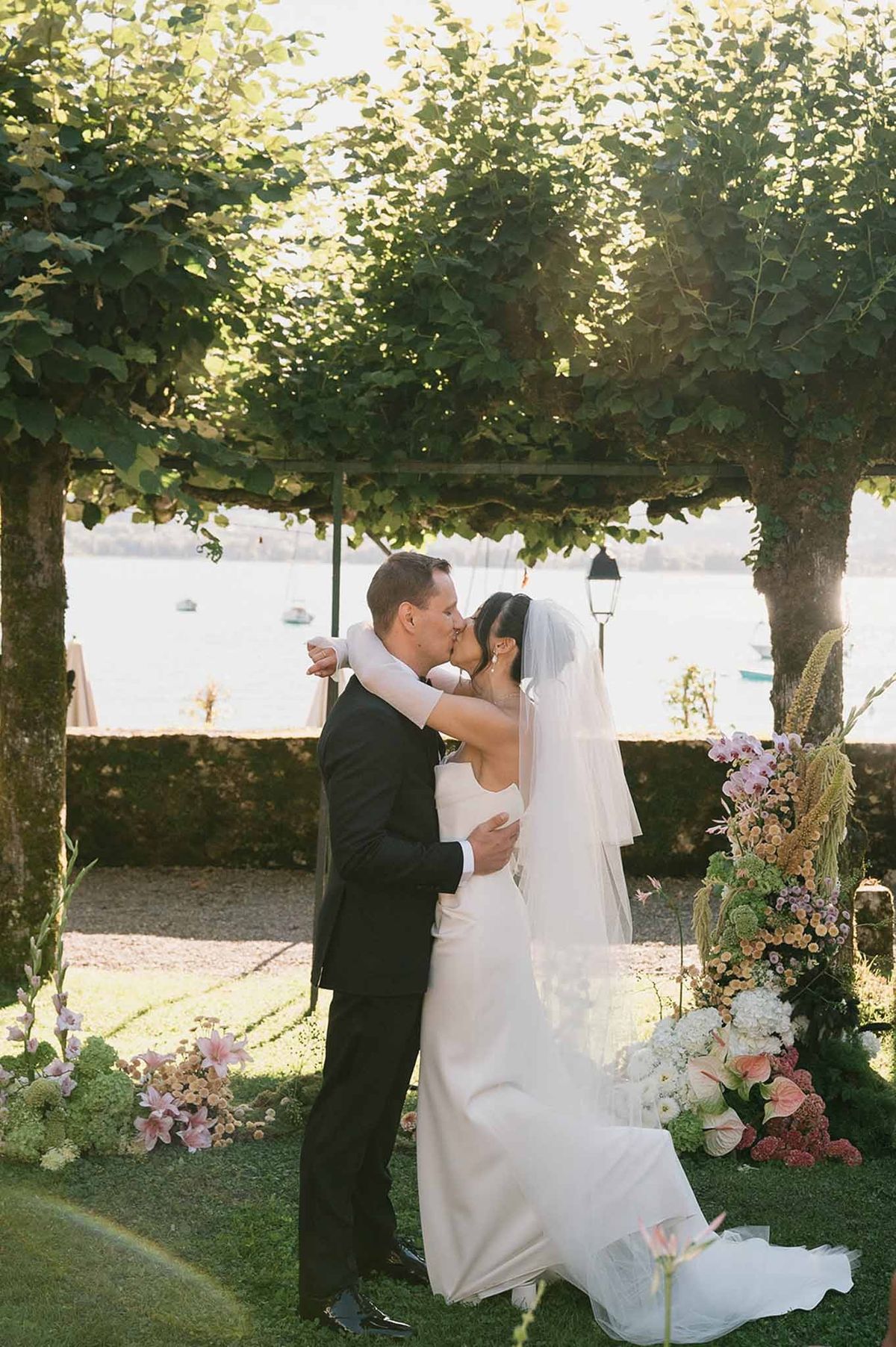 Couple's first kiss at tree altar with lake behind at Abbaye de Talloires