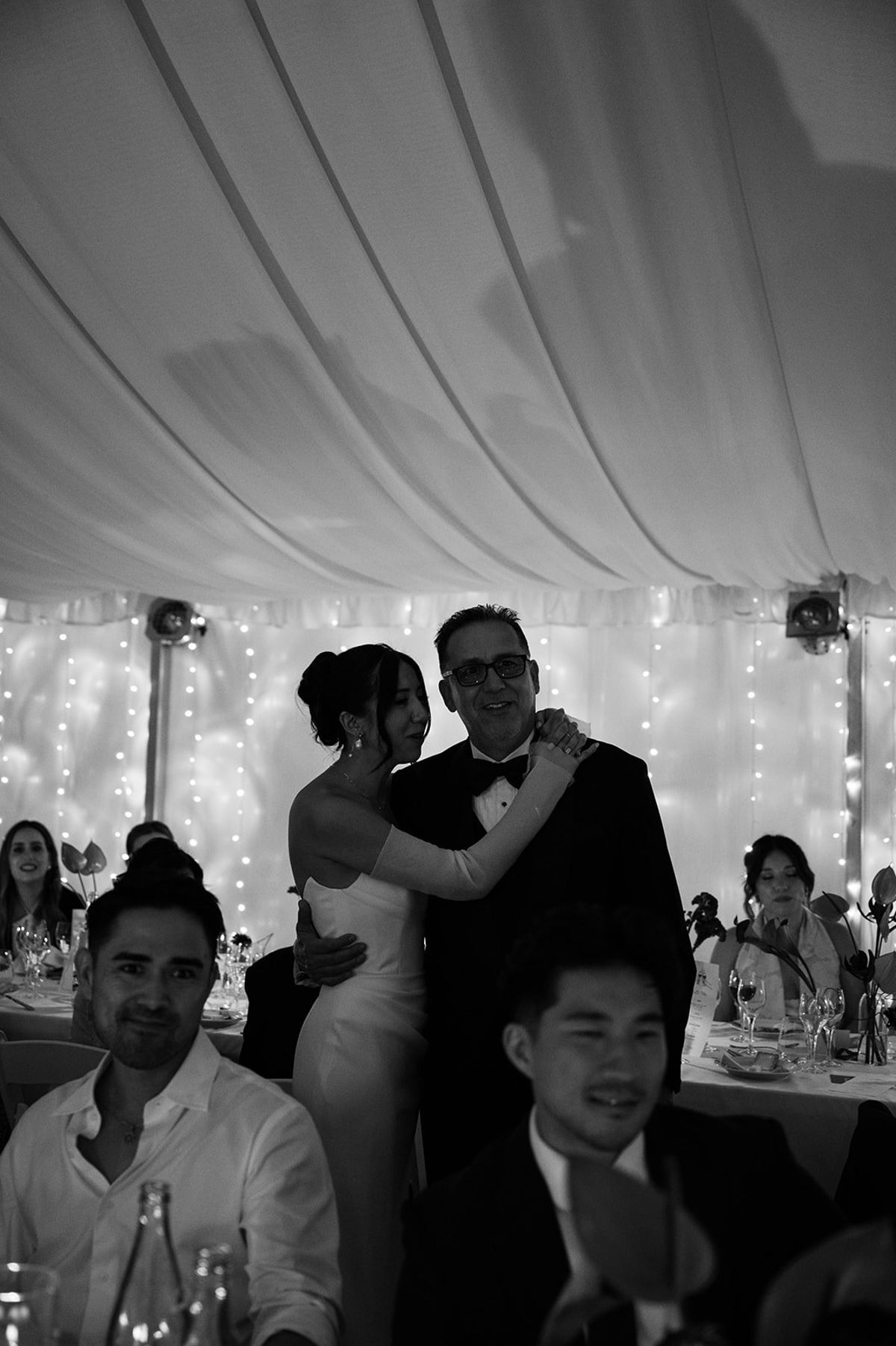 Bride hugs her father beneath fairy lit marquee draping at Abbaye de Talloires