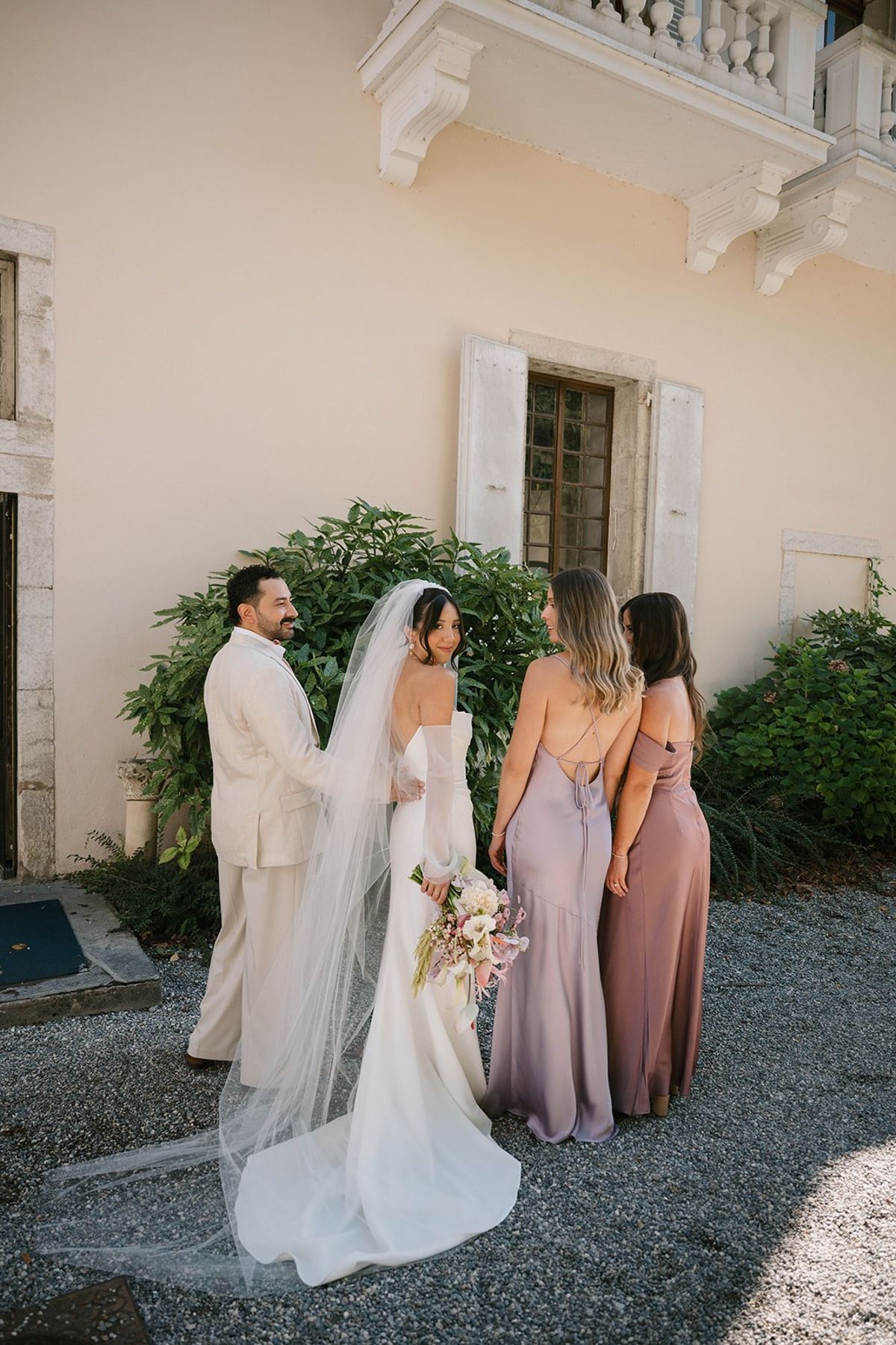 Bride poses with her parents and bridesmaids beside the abbey at Abbaye de Talloires