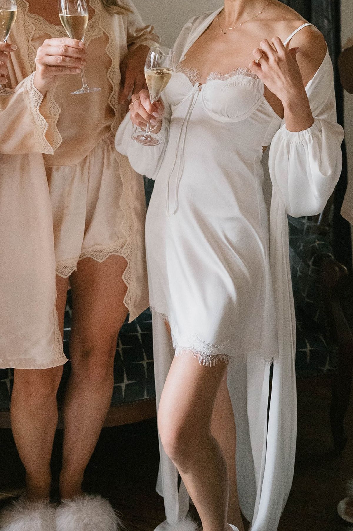 Bride in a lace slip raises a champagne flute beside a bridesmaid at Abbaye de Talloires
