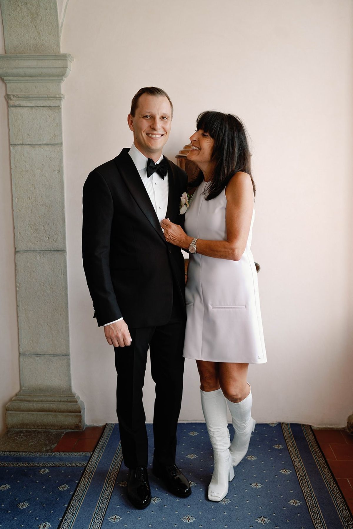 Groom and his mother share a laugh by a stone column at Abbaye de Talloires