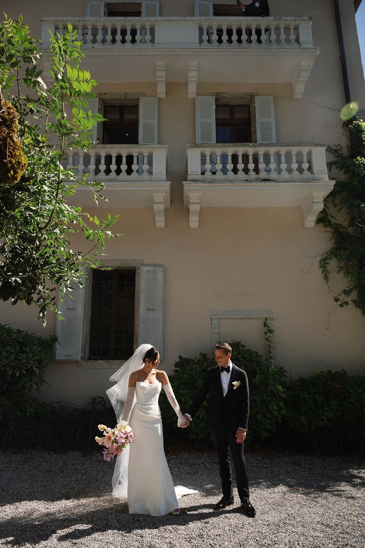 Bride and groom hold hands beneath the abbey's shuttered facade at Abbaye de Talloires