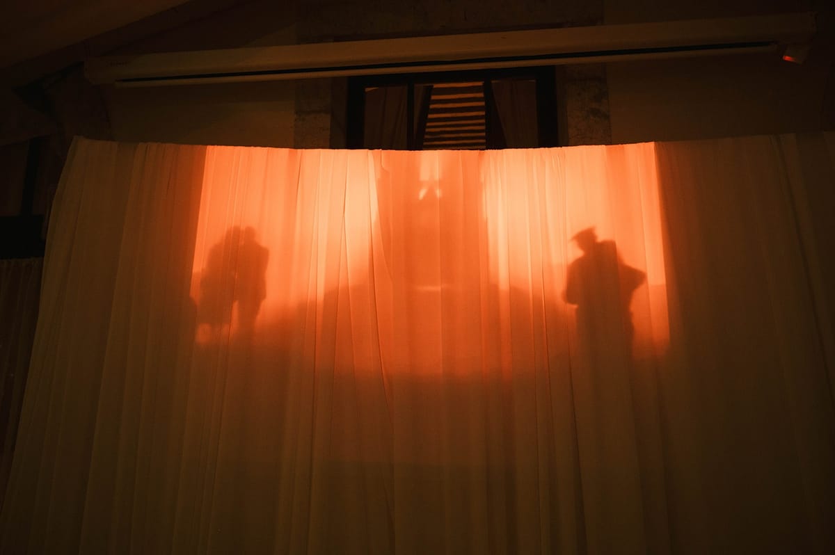 Couple silhouettes glow through amber backlit curtains at Abbaye de Talloires