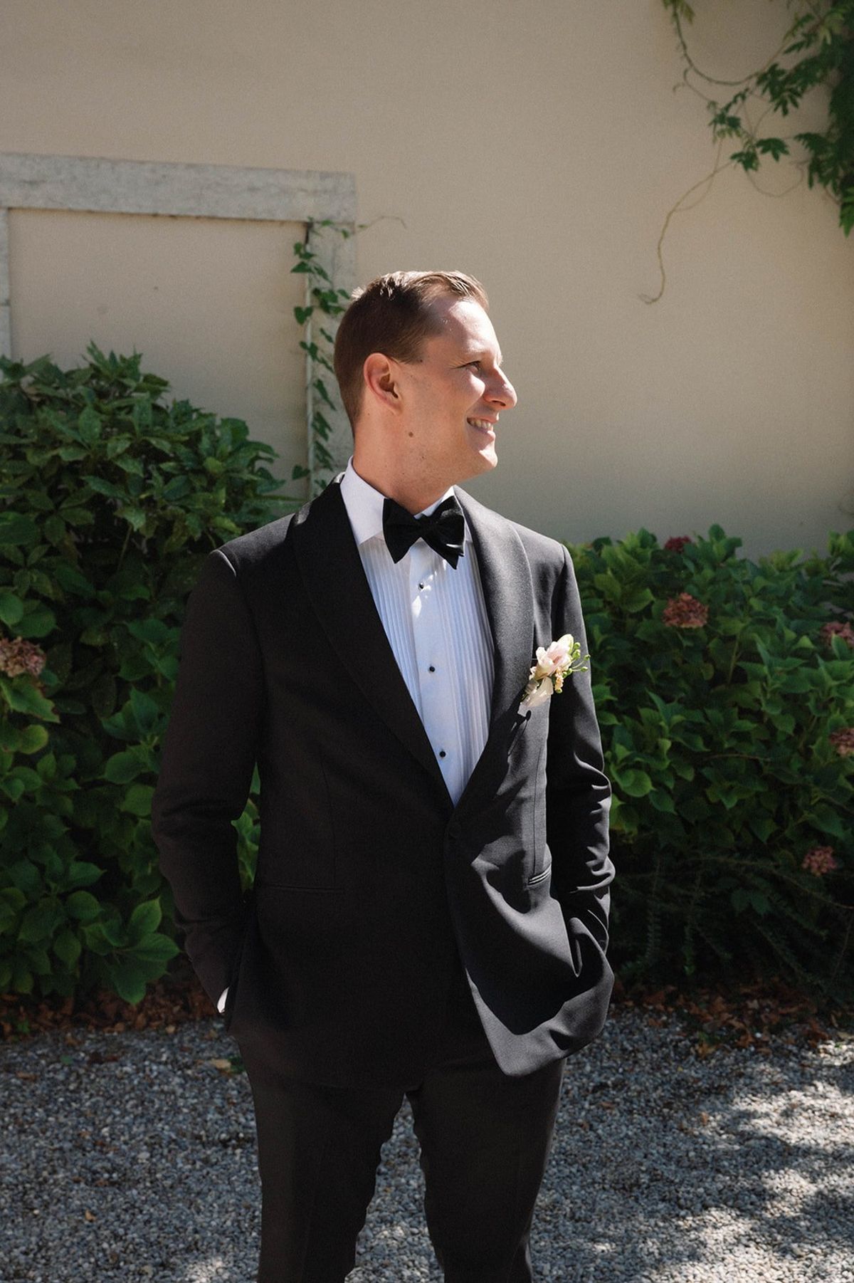 Groom in black tuxedo poses by hydrangeas at Abbaye de Talloires