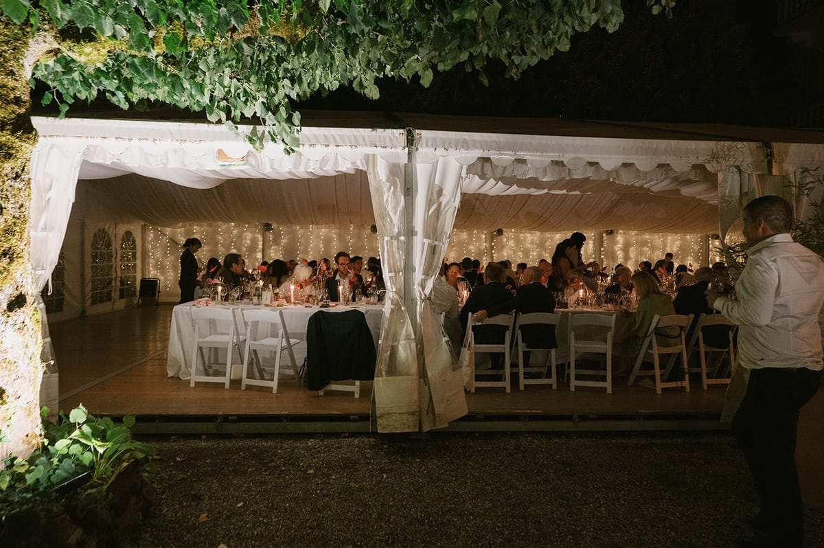 Guests seated at long tables beneath fairy lit marquee draping at Abbaye de Talloires