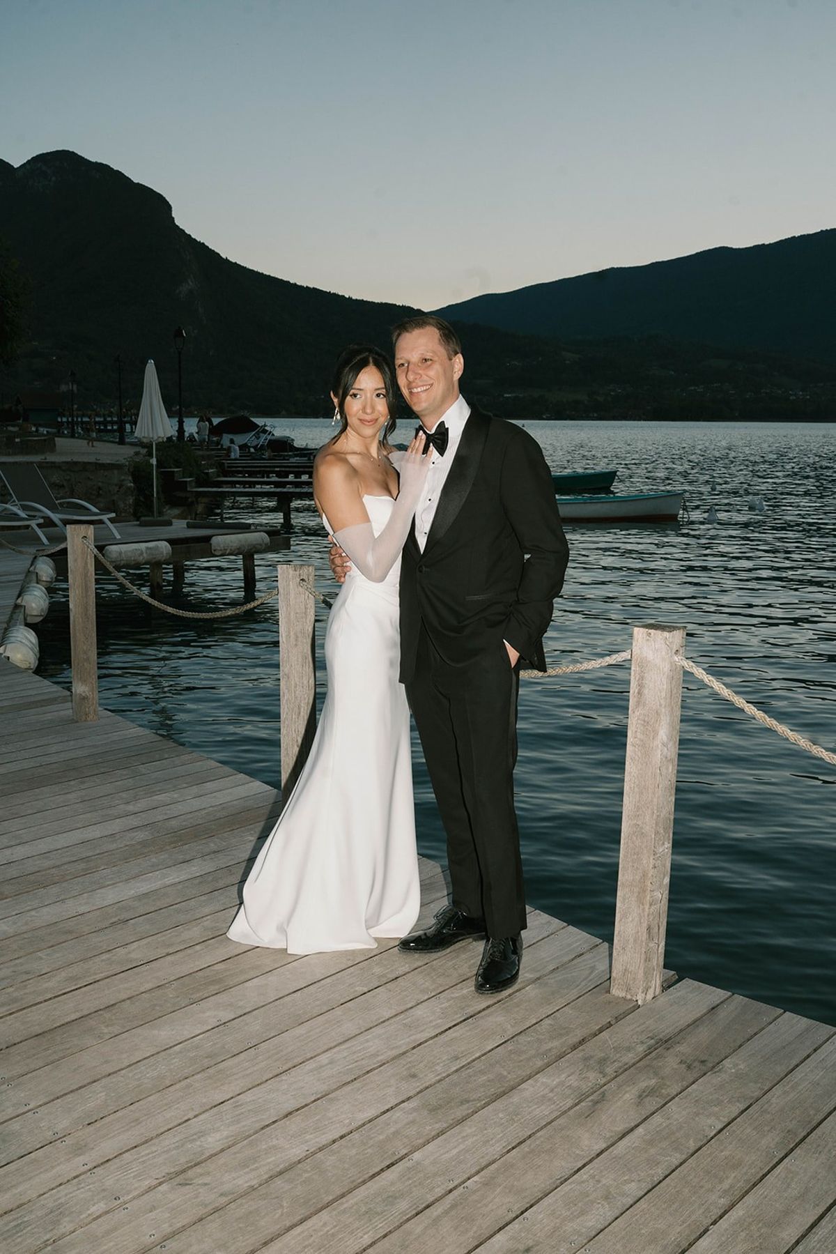 Bride and groom pose on a wooden lake dock with Alpine peaks at Abbaye de Talloires