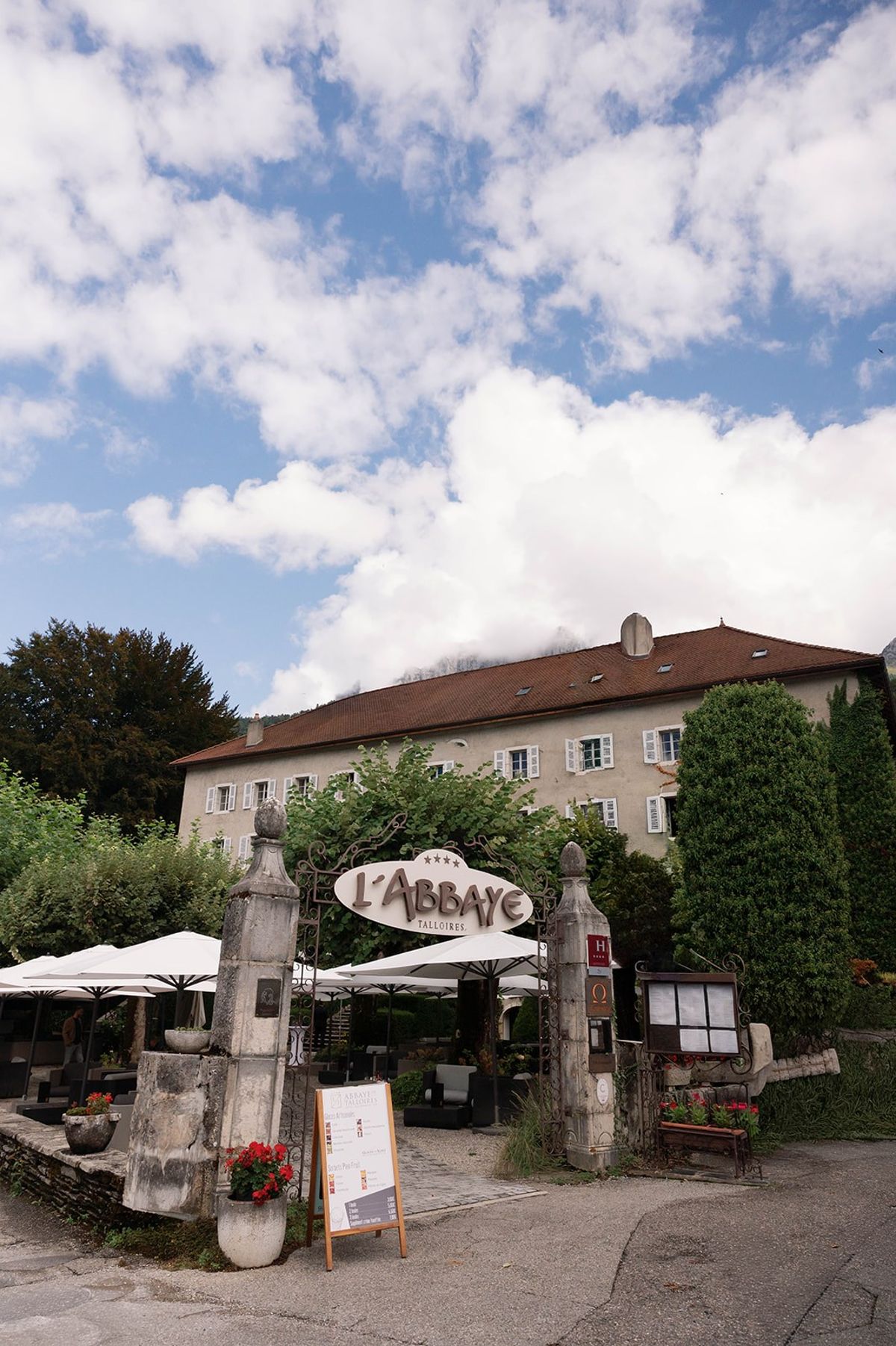 Stone gateway with L'Abbaye de Talloires sign beneath Alpine cloud at Abbaye de Talloires