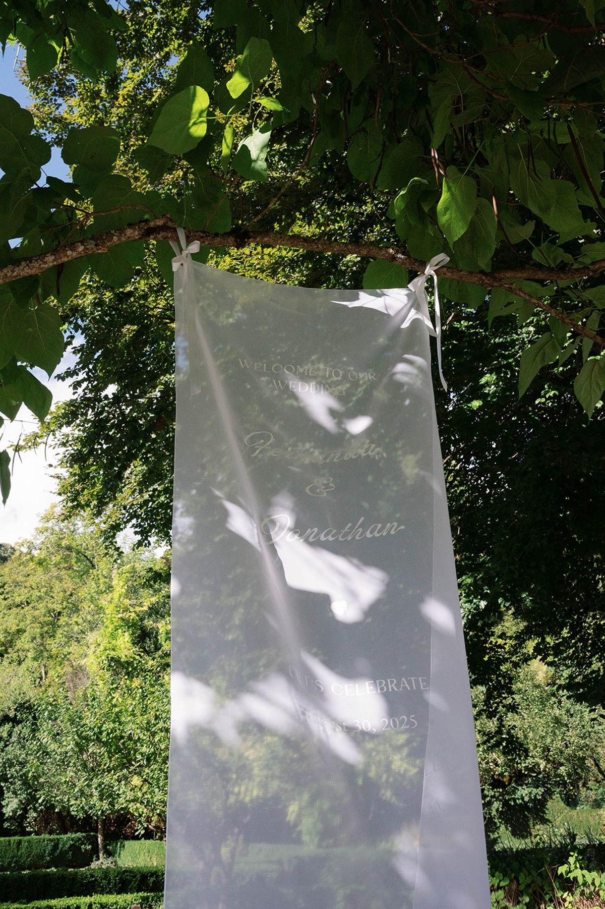 Sheer welcome banner with couple's names hung from a garden tree at Abbaye de Talloires