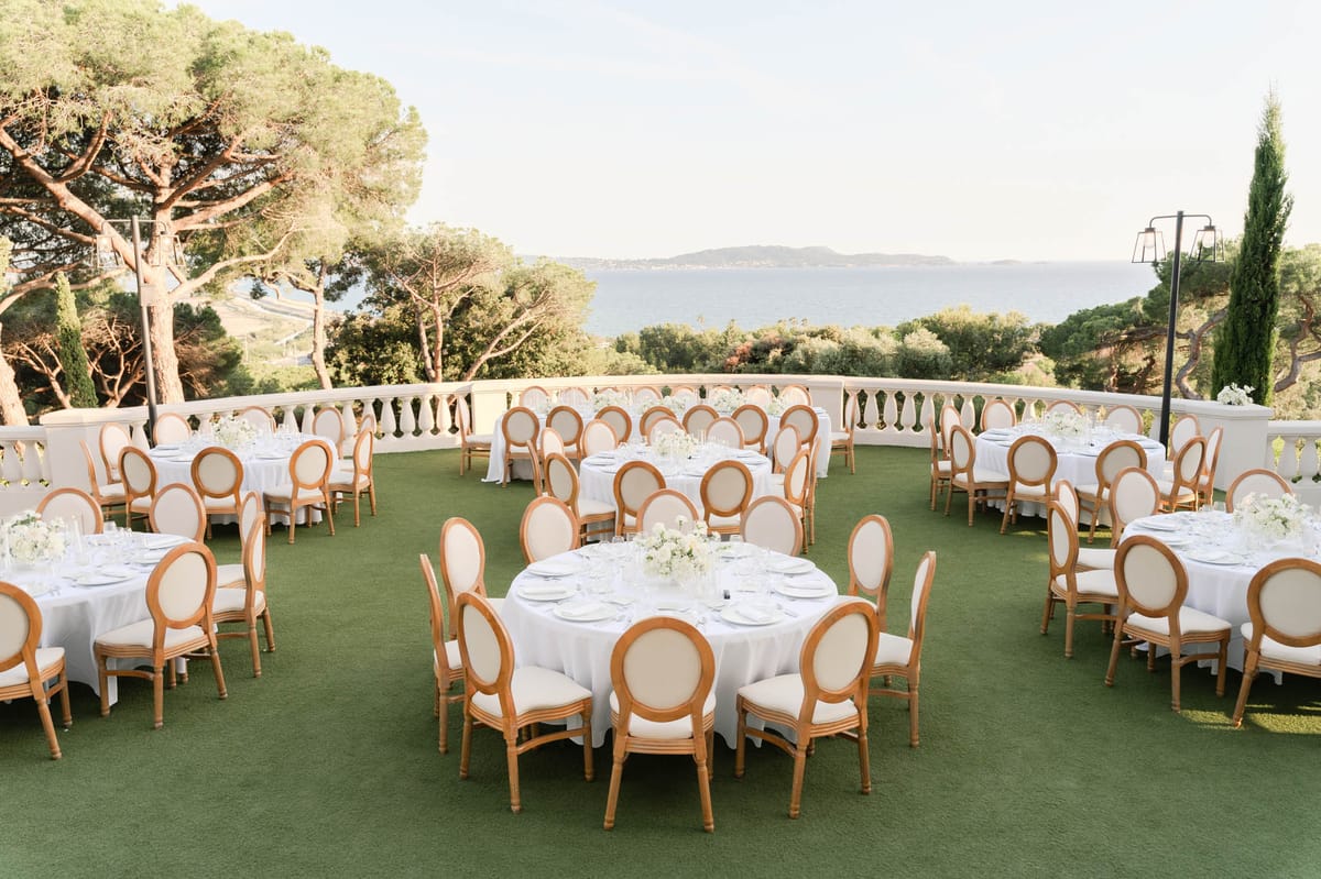 Round tables with white hydrangea centrepieces and Louis XVI chairs on sea-view terrace