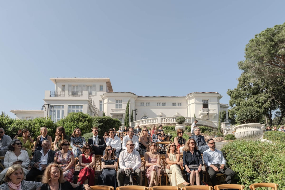Forty guests seated for outdoor ceremony before white rendered villa with cypress trees and balustrades