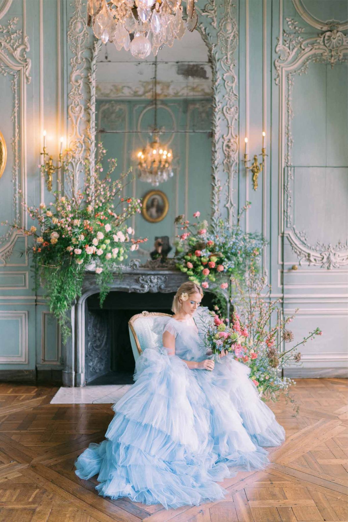 Bride in powder blue tulle gown with coral bouquet flanked by floral installations in Rococo salon