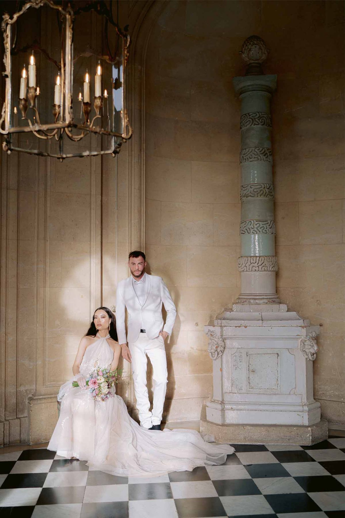 Bride in blush halter gown seated on marble floor with groom in white suit at palace interior