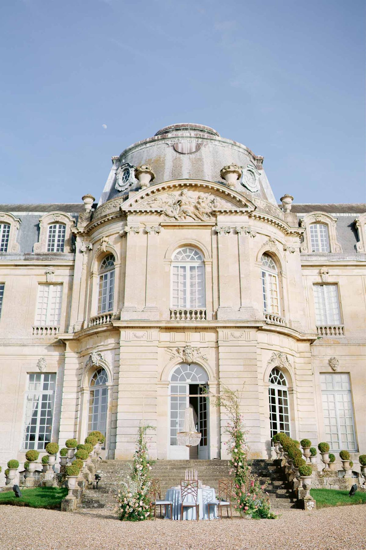 Baroque chateau facade with sweetheart table on forecourt, blush floral installations flanking entrance