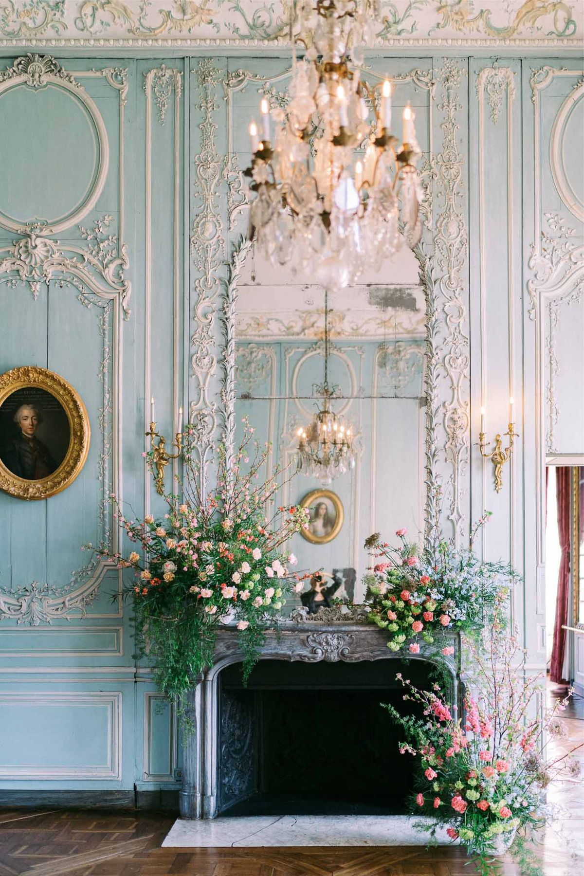 Coral and blush floral installation on fireplace in powder blue boiserie salon with crystal chandelier