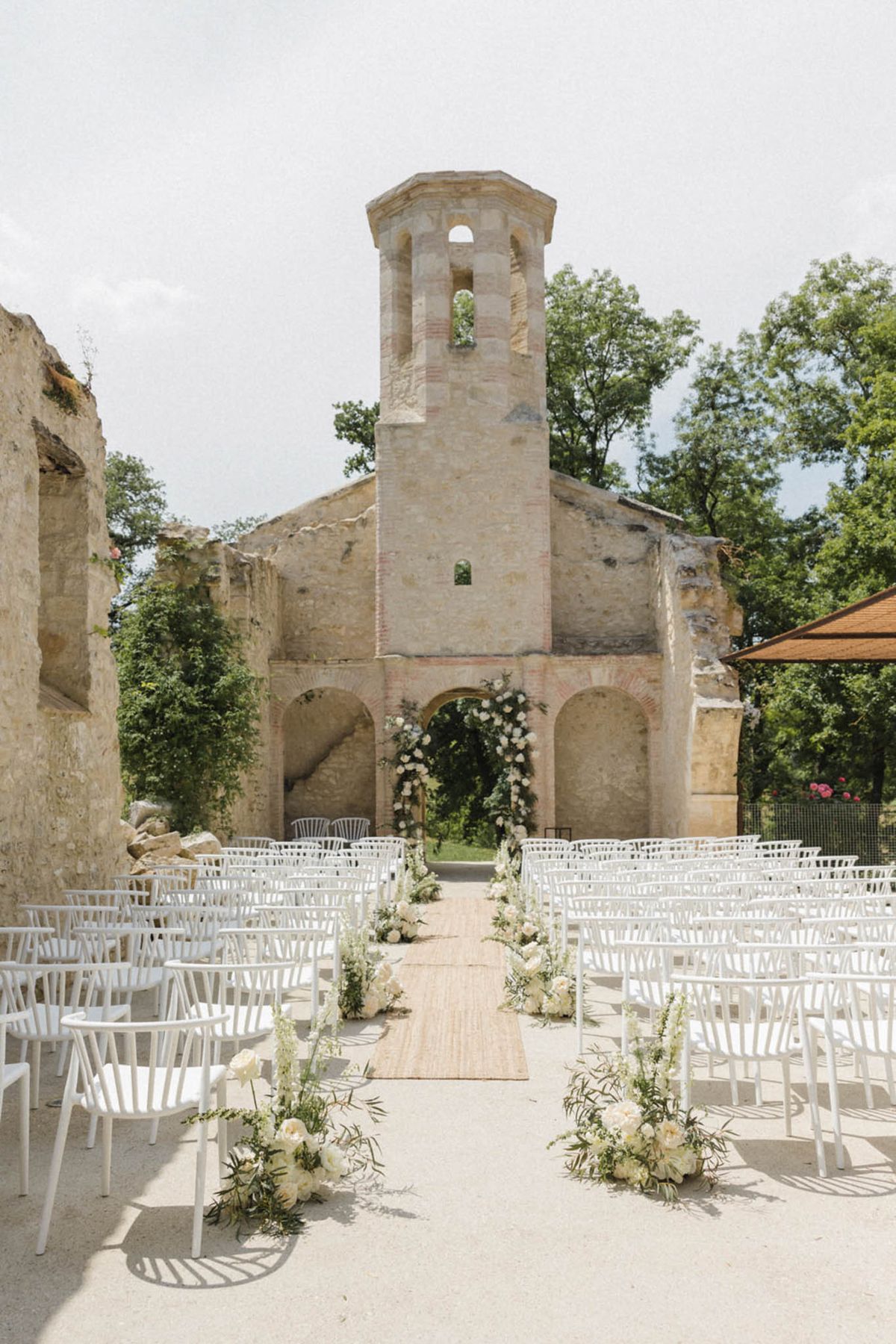 Ceremony in roofless stone chapel ruins with white floral arch and ivory aisle arrangements
