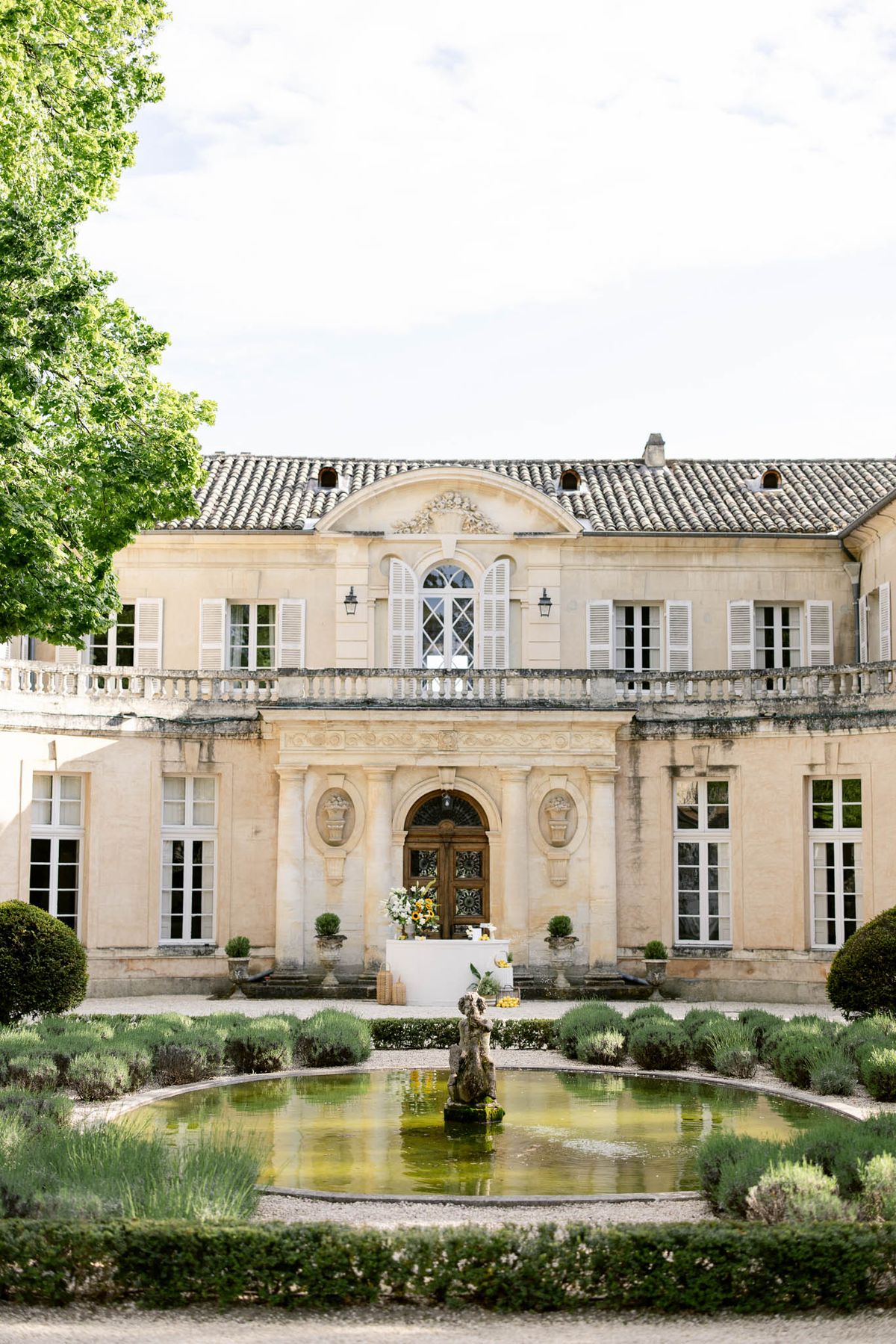 Limestone chateau with terracotta roof and reflecting pool with yellow sunflower welcome display at entrance steps