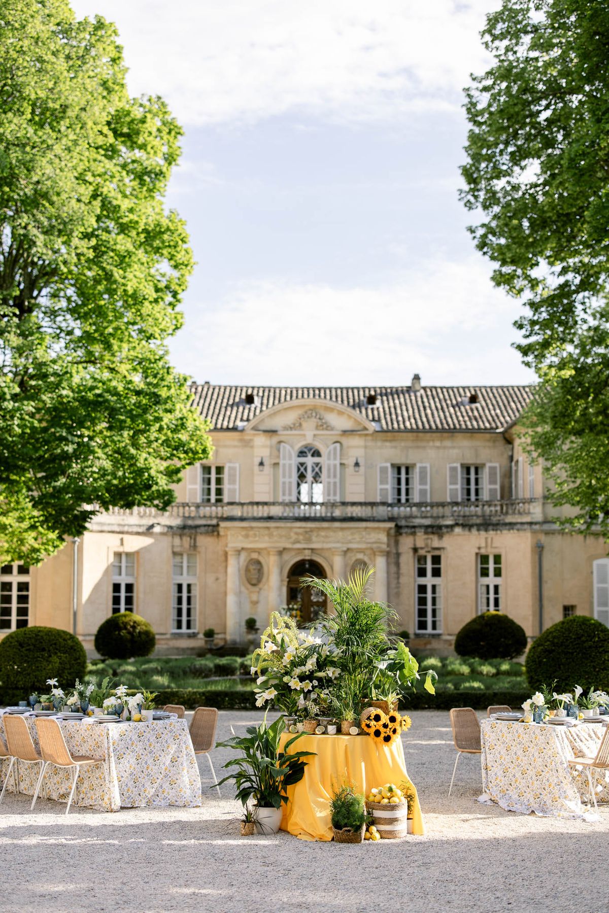 Yellow linen centrepiece table with sunflowers and lemons before limestone chateau with topiary