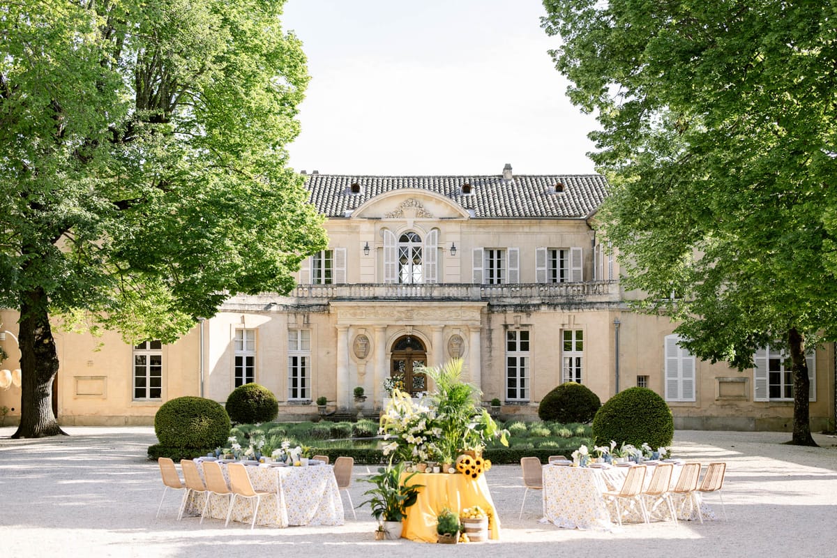 Round tables with floral linens and rattan chairs in chateau courtyard with yellow and sunflower centerpiece display