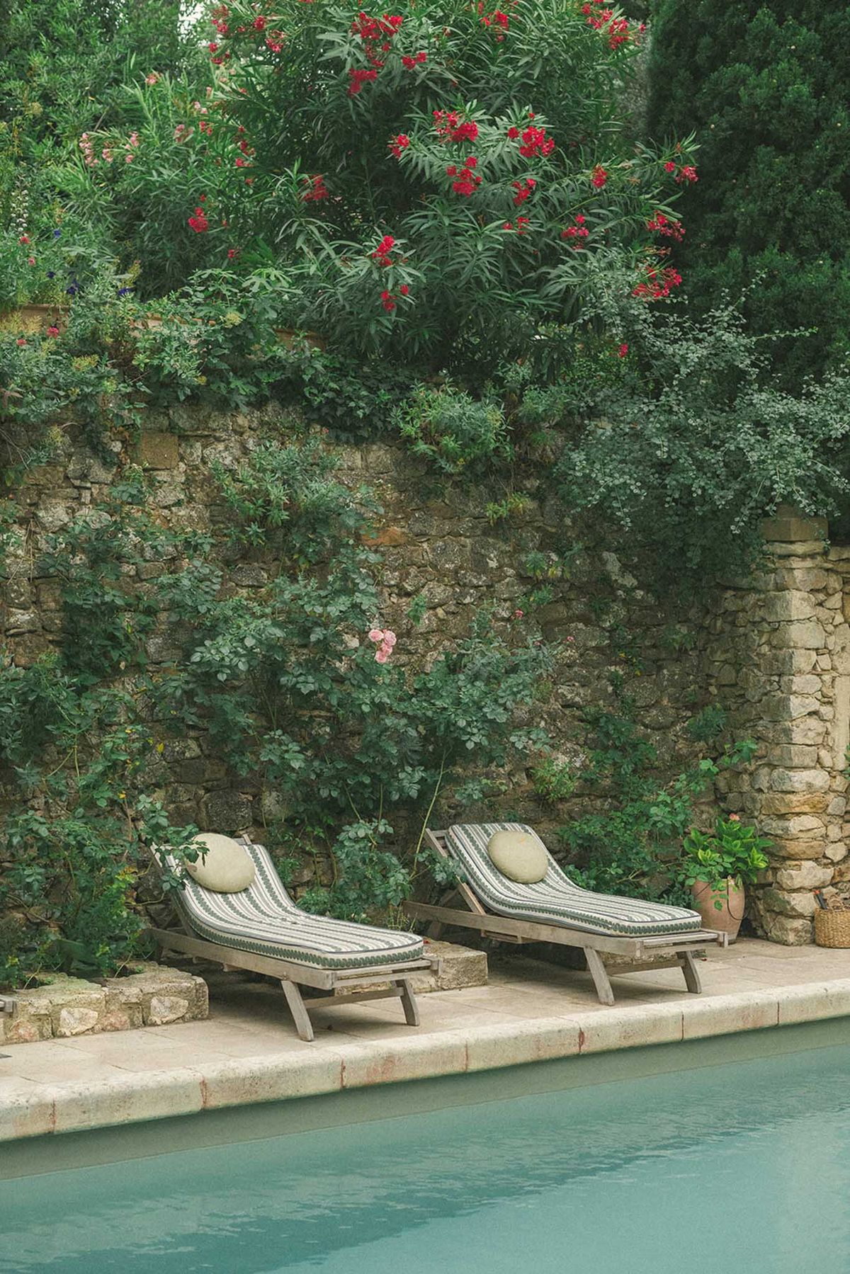 Pool terrace with green-striped loungers, stone wall with climbing plants, and teal-green pool water
