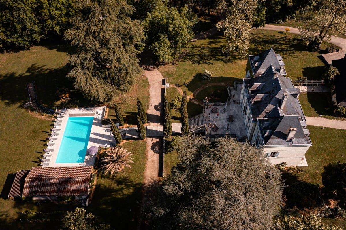 Aerial chateau with slate mansard towers, turquoise pool with cypress trees, and sweeping lawn grounds
