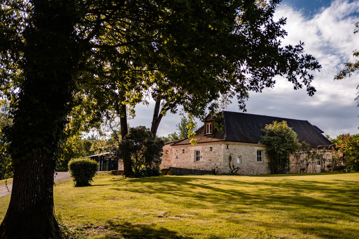 Stone countryside building with dark slate roof and mature tree beside modern glass-and-steel extension