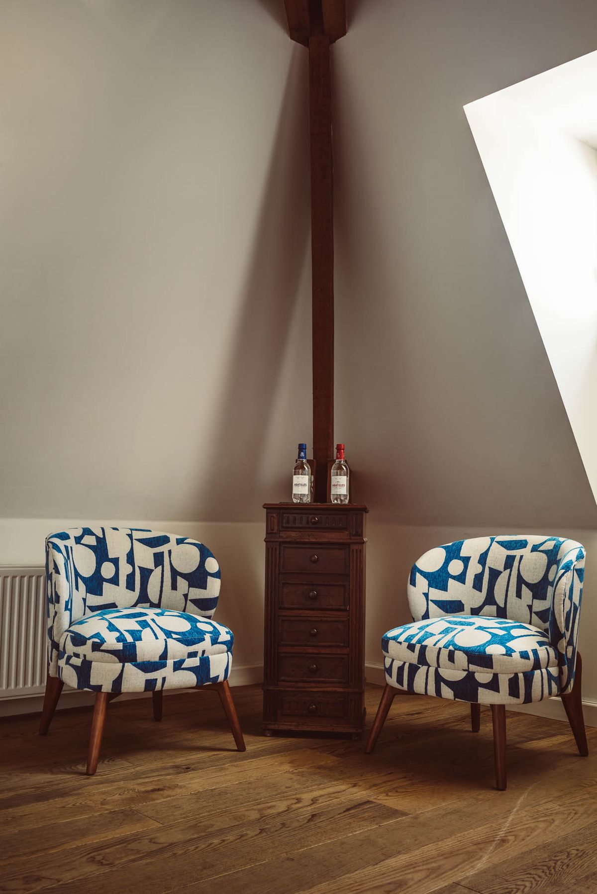 Attic room with blue geometric armchairs, dark wood chest, skylight, and herringbone parquet floor
