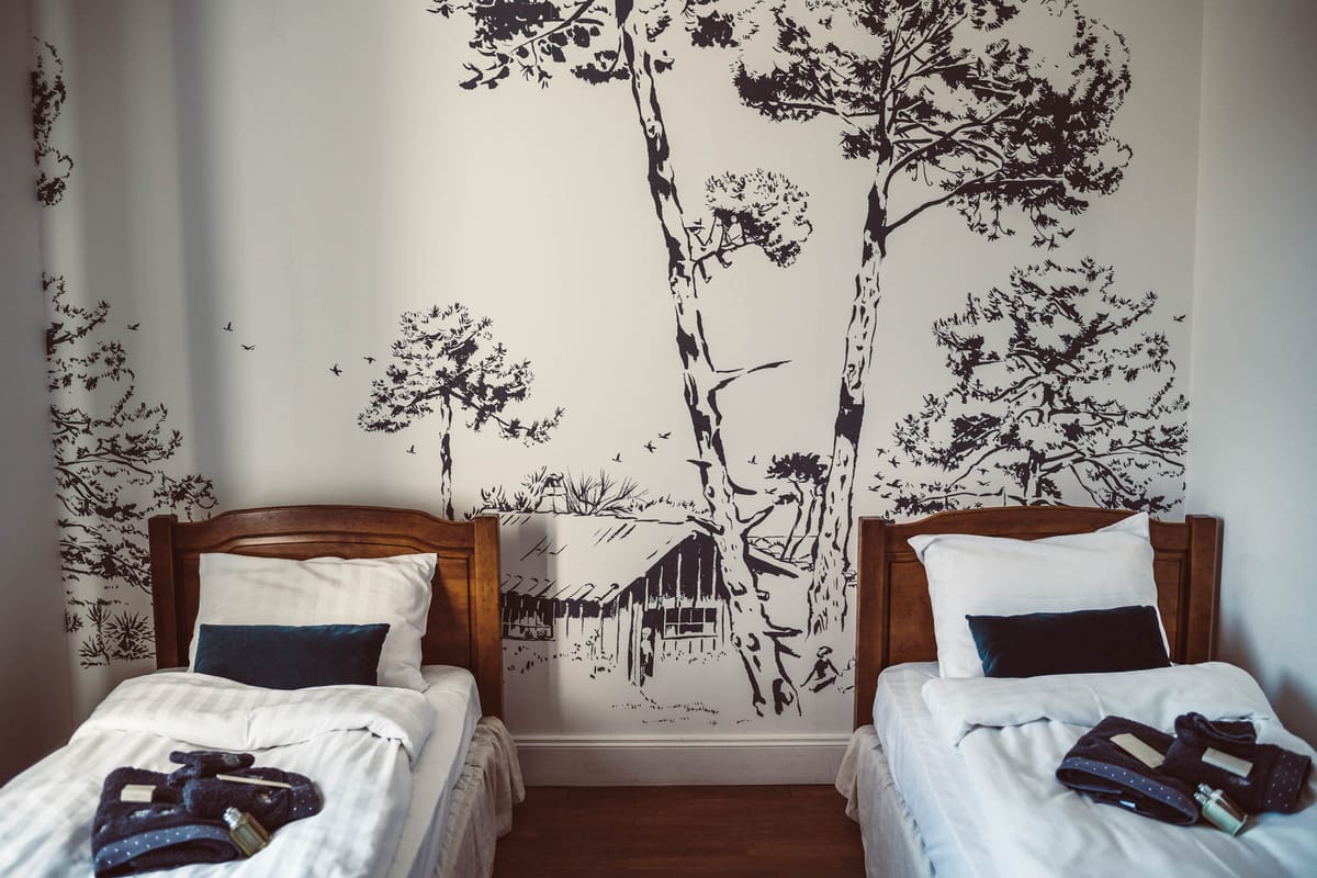 Twin guest beds with navy accents and polka-dot robes beneath large-scale black ink forest mural