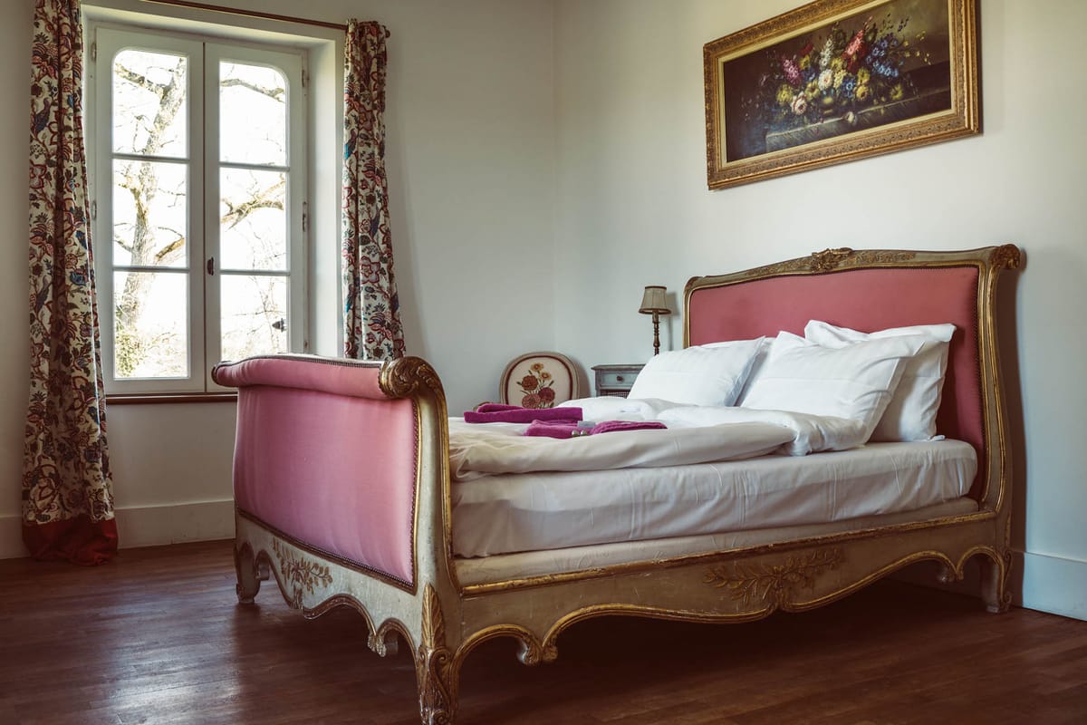 Chateau bedroom with gilded Louis XV sleigh bed, rose-pink upholstery, floral toile curtain, and hardwood floor