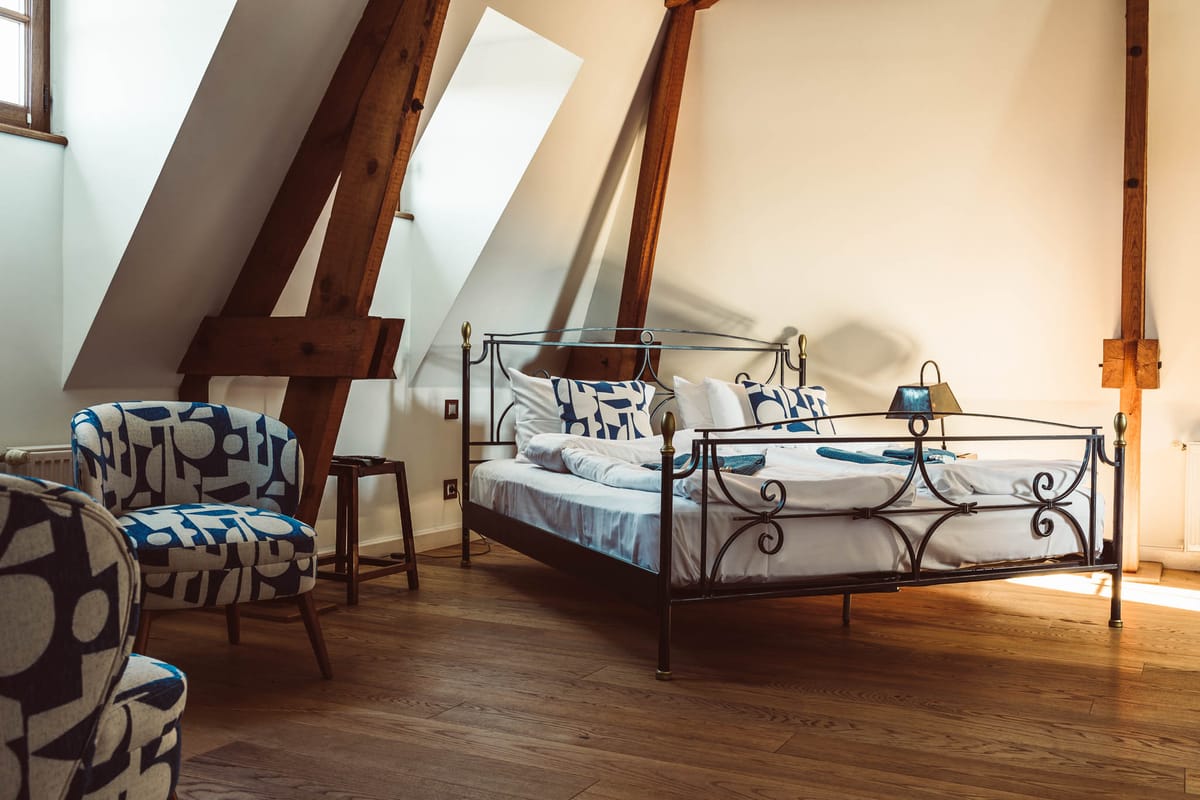 Attic guest bedroom with exposed dark wood beams, wrought-iron bed, navy geometric cushions, and skylight