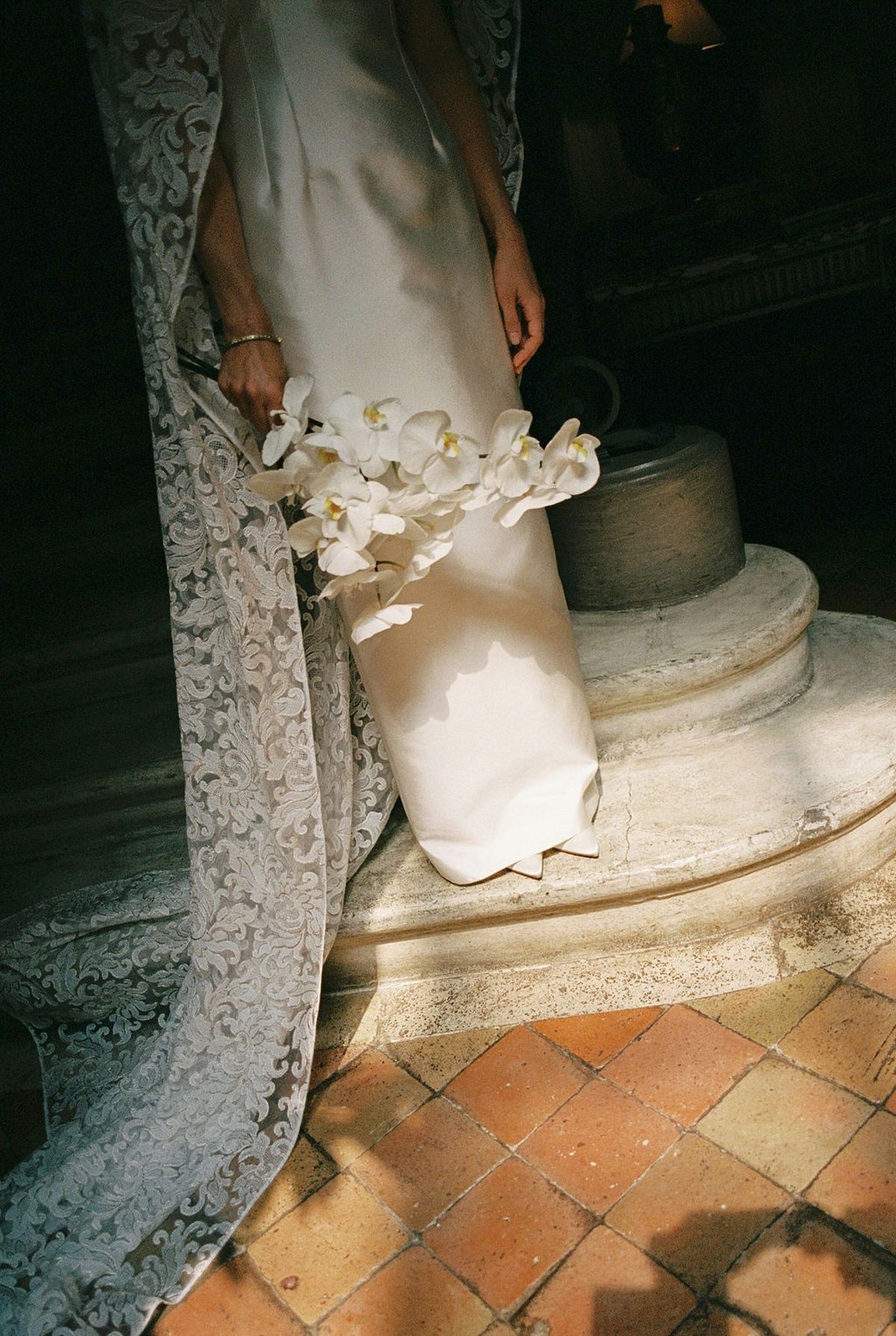 White orchid bouquet against silk wedding dress and lace cape on stone step