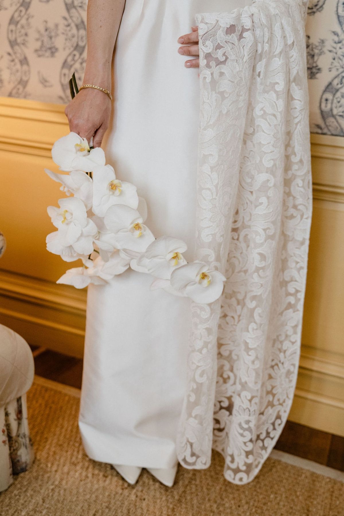 Bride holding cascading white orchid bouquet against silk dress with lace cape