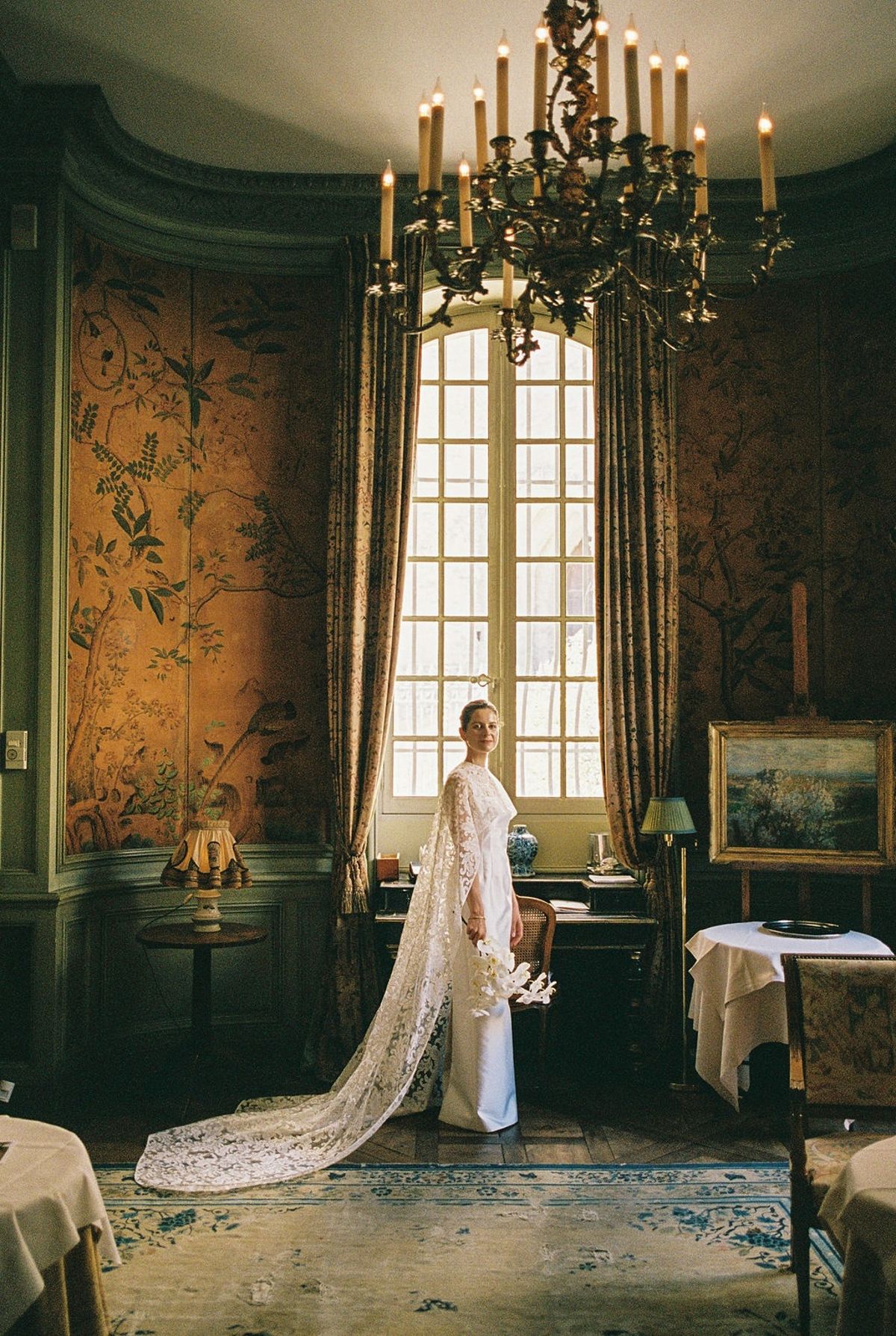 Bride at arched chateau window with orchid bouquet and lace train pooling