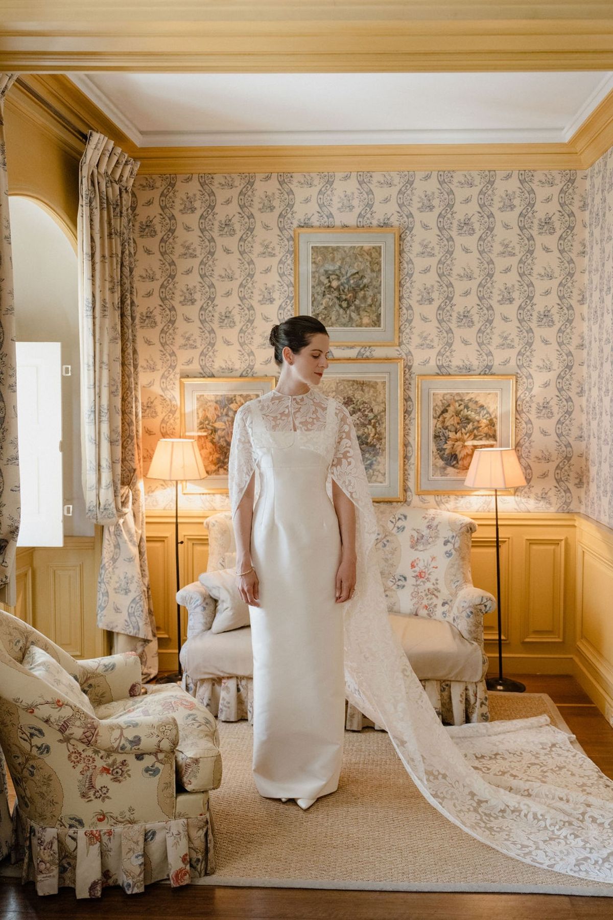 Bride in silk dress with lace cape trail in yellow-panelled chateau salon