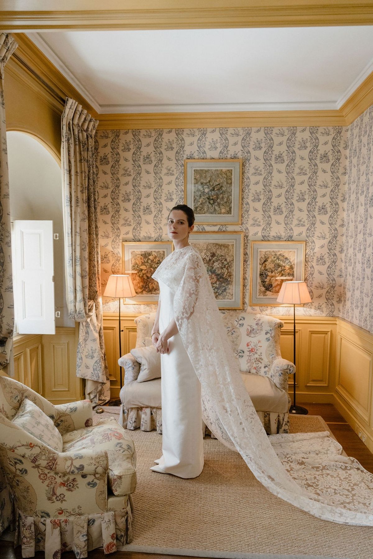 Bride in lace cape sweeping wide arc in toile-papered chateau salon