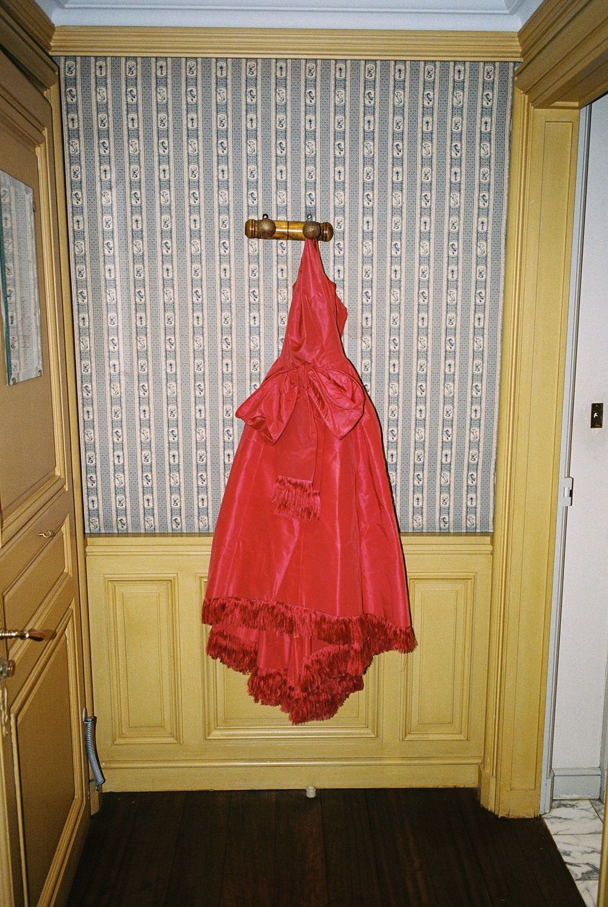 Red taffeta evening gown with bow and fringe hem hanging on vintage wallpaper