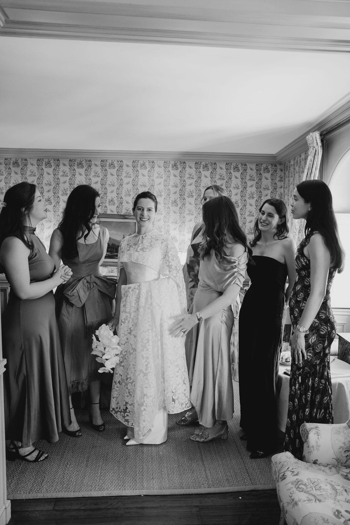 Bride with bridesmaids in chateau bedroom holding orchid bouquet in black and white
